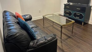 Ett vardagsrum med en svart lädersoffa, ett soffbord i glas och en TV-bänk med en platt-TV.