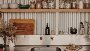 Una cucina con lavello in acciaio inossidabile, tagliere in legno, barattoli sugli scaffali e diversi utensili.