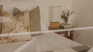 Una camera da letto con un letto, cuscini a quadretti, un comodino con un vaso e un libro.