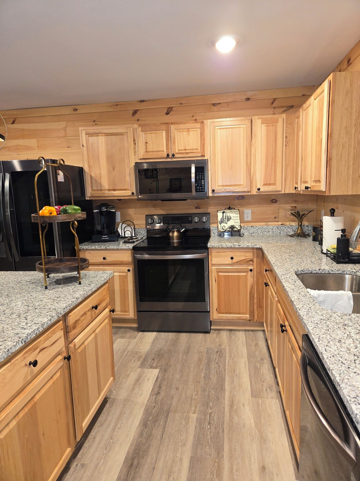 A kitchen with wooden cabinets, a stainless steel refrigerator, a microwave, an oven, and granite countertops.