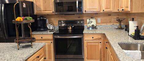 A kitchen with wooden cabinets, a stainless steel refrigerator, a microwave, an oven, and granite countertops.