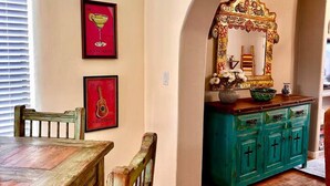 Un comedor con una mesa y sillas de madera, un armario azul verdoso con espejo, y dos cuadros en la pared.