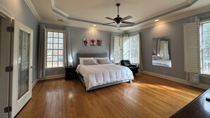 A bedroom with a large bed, a ceiling fan, and multiple windows with shutters.