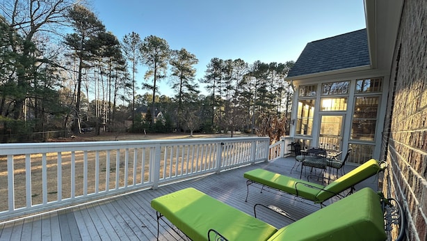 A covered outdoor deck with two green lounge chairs, a table, and chairs.