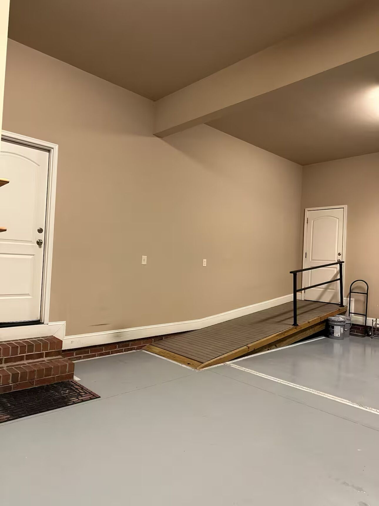 A room with a ramp leading to a door, a small step with a handrail, and a ladder against the wall.