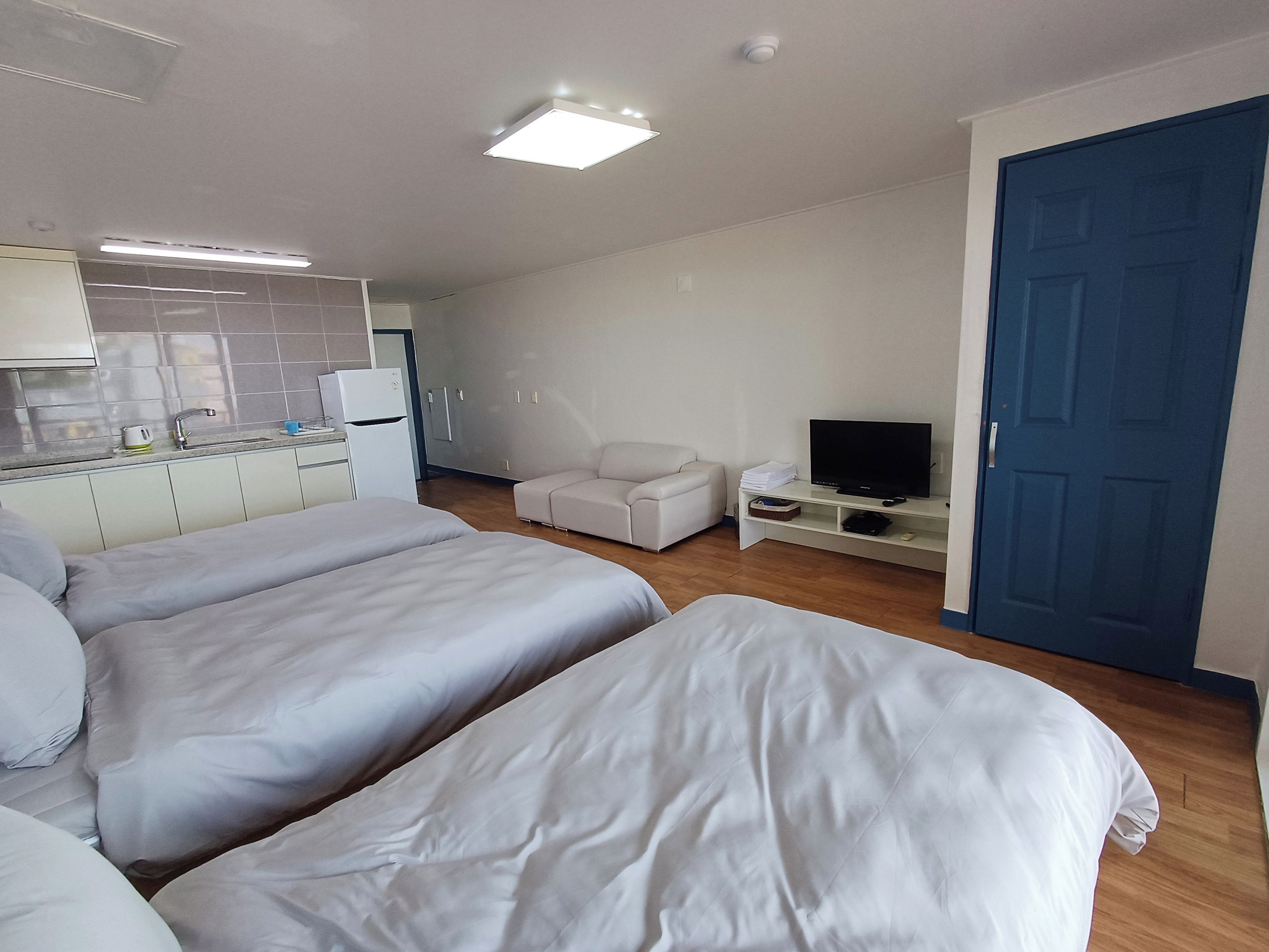 Habitación de hotel con dos camas, kitchenette, televisor y una puerta azul.
