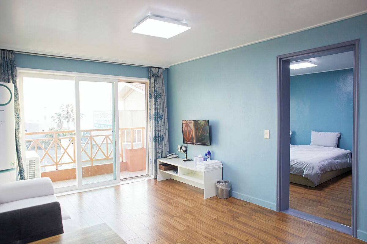 A room with a bed, a desk with a computer, a TV, and a balcony with a view.