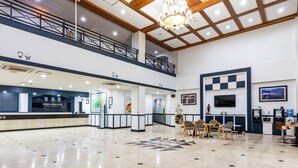 A spacious lobby with a high ceiling, a chandelier, a reception desk, and a seating area with chairs and tables.