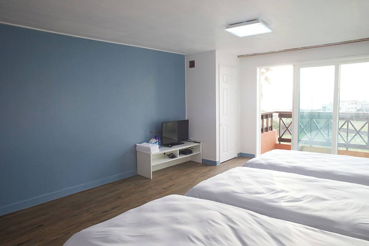 A hotel room with two beds, a desk with a TV, and a balcony with a view.