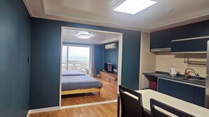 A room with a bed, a desk, a chair, a kitchenette, and a view of the outside.