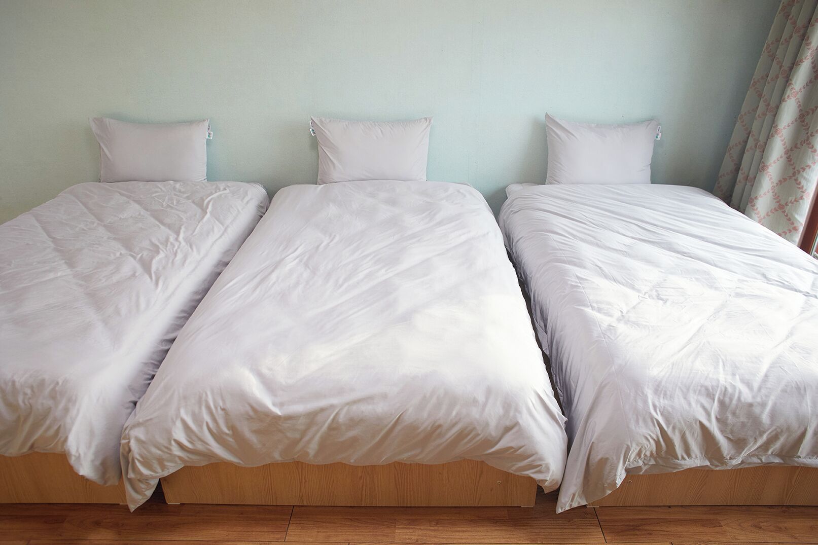 A room with three single beds aligned against a light-colored wall.