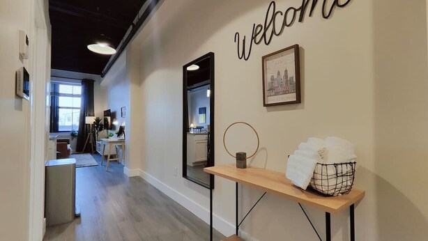 A modern interior with a 'Welcome' sign, a framed cityscape picture, and a small table with a basket of towels. - Studio Apt Near Temple Unit with Free Parking for Extended Stays (Philadelphia)