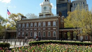 A historic building with a clock tower, surrounded by a garden of tulips and a flag. - Studio Apt Near Temple Unit with Free Parking for Extended Stays (Philadelphia)