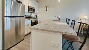 A modern kitchen with white cabinets, stainless steel appliances, a granite countertop, and a central island with bar stools. - Studio Apt Near Temple Unit with Free Parking for Extended Stays (Philadelphia)