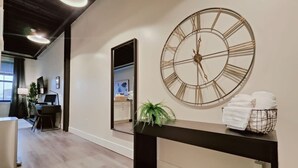 A modern interior with a large wall clock, a mirror, and a console table with towels. - Cozy Philly Studio with Free Parking for Long Term Stays (Philadelphia)