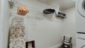 A laundry room with a washing machine, a drying rack, and a shelf with hanging clothes and a basket. - Cozy Philly Studio with Free Parking for Long Term Stays (Philadelphia)