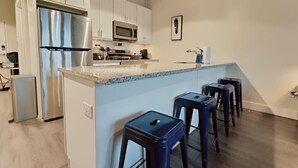 A modern kitchen with white cabinets, stainless steel appliances, a granite countertop, and a bar stool seating area. - Cozy Philly Studio with Free Parking for Long Term Stays (Philadelphia)