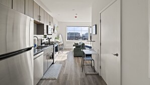 A modern kitchen with stainless steel appliances, a dining area with a table and chairs, and a large window offering a city view. - Boutique Studio with Rooftop View and Gym (Philadelphia)
