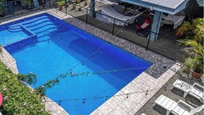Et rektangulært swimmingpool med fliseterrasse, omgivet af plantekrukker og udendørs møbler.