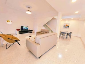 Una sala de estar moderna con un sofá, un televisor, una mesa de comedor con sillas y una escalera.