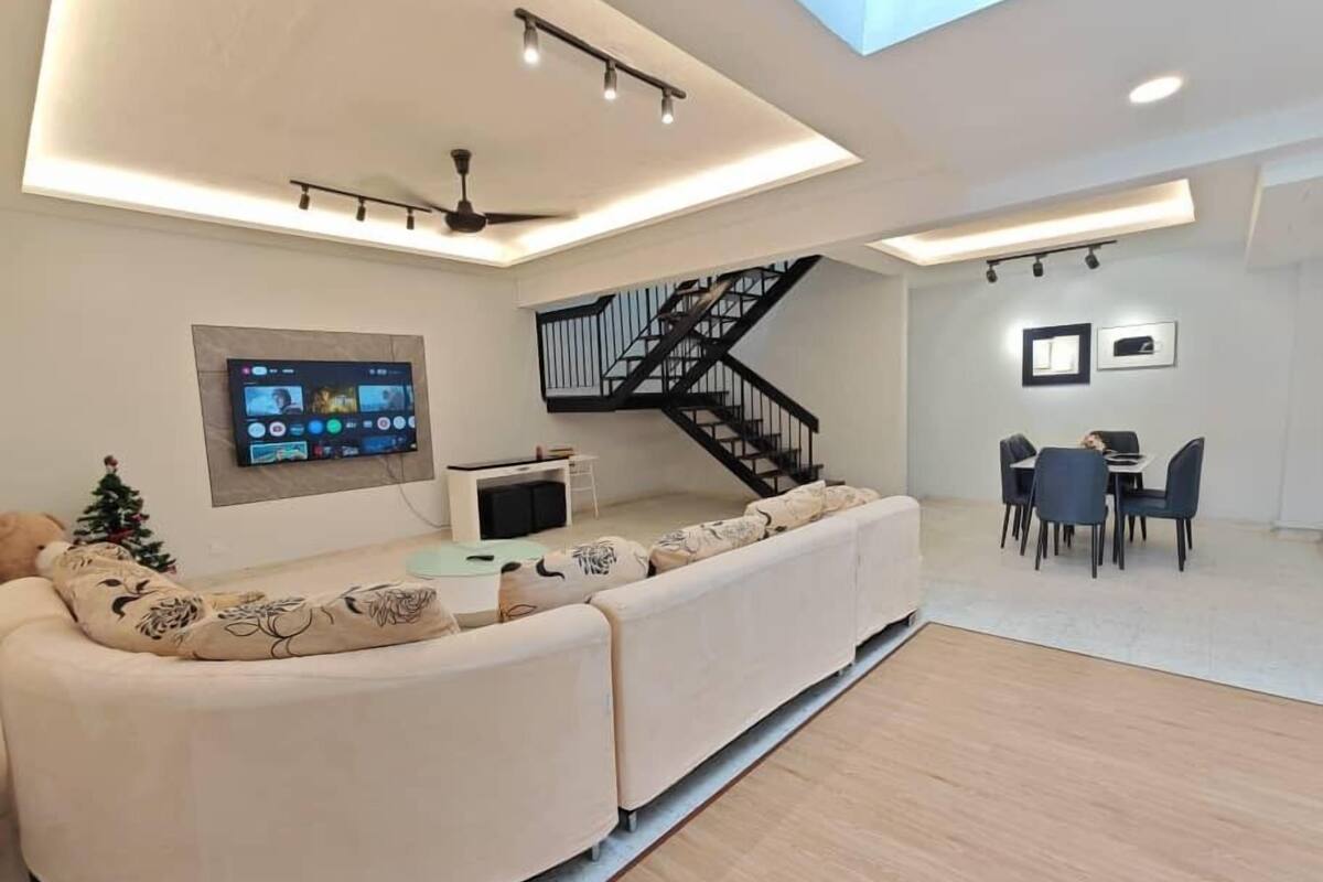 Una sala de estar moderna con un sofá curvo, un televisor de pantalla plana, una escalera y un comedor.