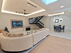 Una sala de estar moderna con un sofá curvo, un televisor de pantalla plana, una escalera y un comedor.
