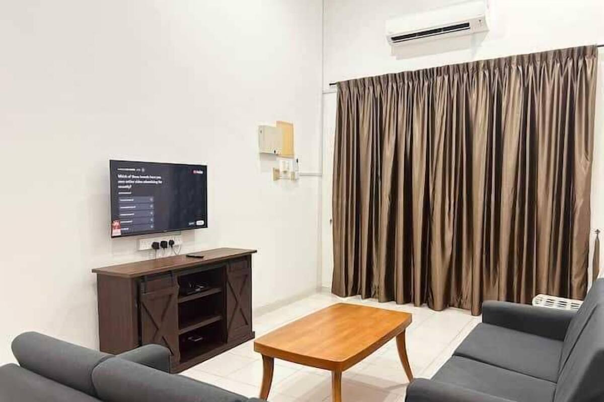 Una sala de estar con un televisor de pantalla plana, una mesa de centro de madera y dos sofás grises.