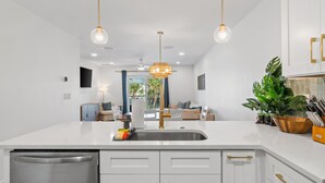 Una cocina moderna con armarios blancos, un lavamanos de acero inoxidable e iluminación colgante.