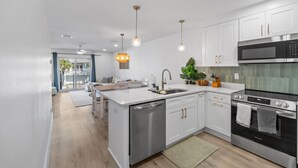 Una cocina moderna con armarios blancos, electrodomésticos de acero inoxidable, iluminación colgante y vistas a un balcón.
