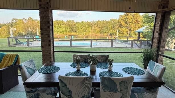 A dining area with a view of a backyard pool and trees.