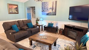 A living room with a brown leather sofa, a wooden coffee table, a flat-screen TV, and a fireplace.