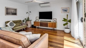 Ein modernes Wohnzimmer mit einer Ledersofa, einem grünen Sofa, einem Flachbildfernseher, einem Deckenventilator und einer großen Topfpflanze.
