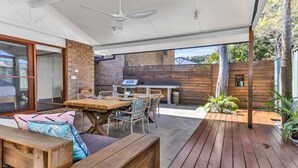 Eine Terrasse im Freien mit Holzboden, einem Esstisch mit Stühlen und einer Grillgegend.