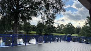 A wooden deck with a blue railing overlooking a body of water, surrounded by trees and a grassy area. - Charming 2-bedroom townhome in Winter Springs. (Winter Springs)