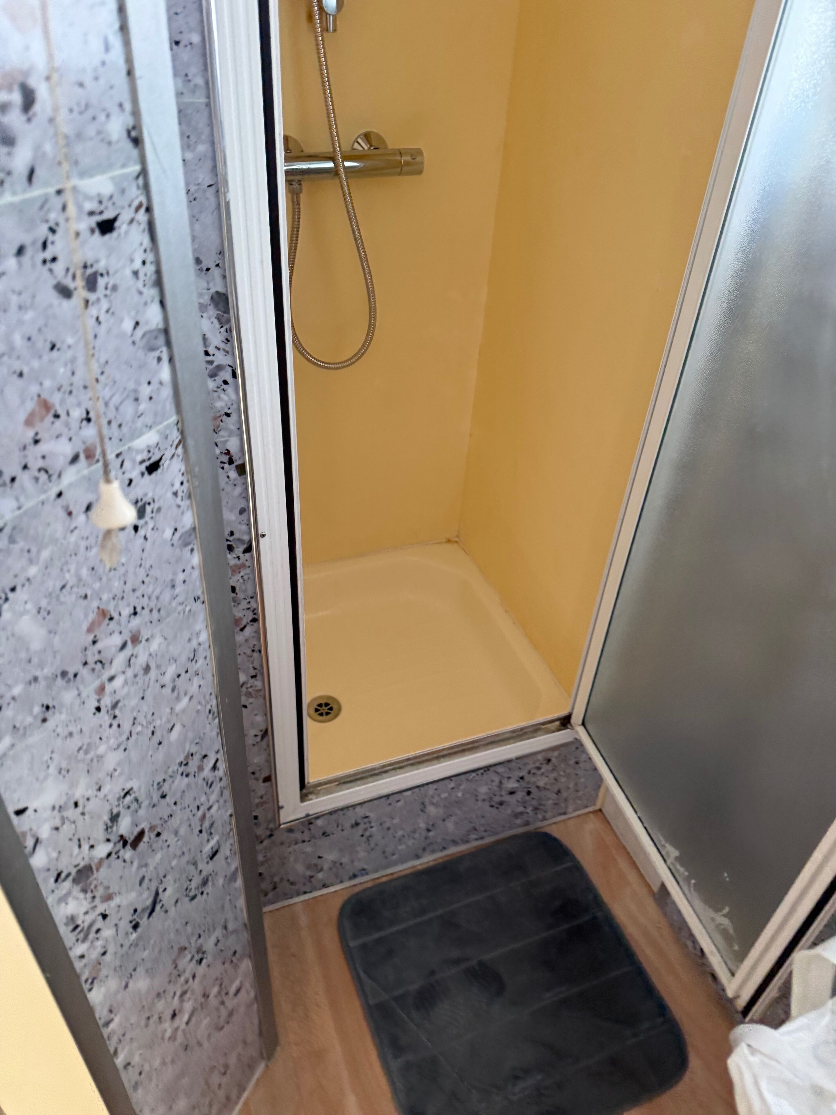 Un petit espace douche fermé, avec un mur jaune et une porte en métal.