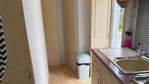 A compact kitchen with wooden cabinets, a sink, and a small trash bin.