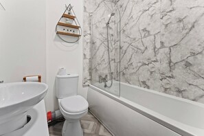A bathroom with a toilet, a sink, a shower with a glass enclosure, and a marble wall.