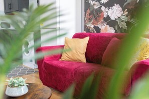 A red sofa with a beige pillow in a room with a washing machine and a floral wall mural.