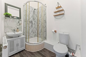 Een badkamer met een douchecabine met gebogen wanden, een witte wastafel, een toilet en een houten plankje met een decoratief object.