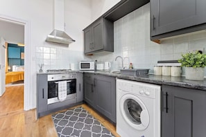 Een compacte keuken met grijze kastjes, een ingebouwde magnetron, een wasmachine en een klein spoelbakje.