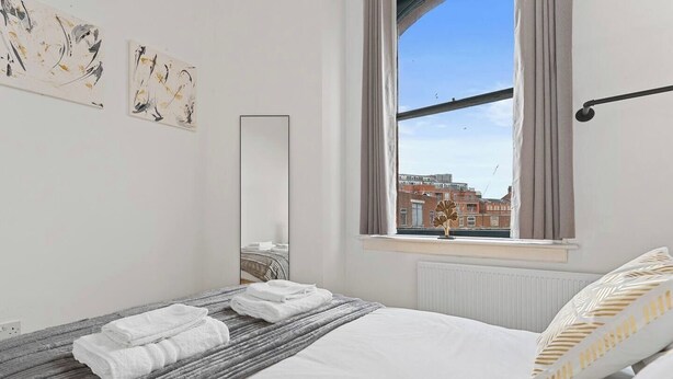 Ein Hotelzimmer mit einem Bett, einem Fenster mit Blick auf Gebäude und Kunstwerken an der Wand.