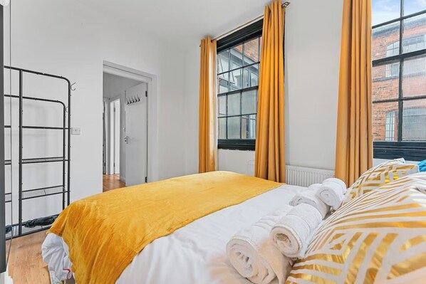 A hotel room with a bed, a window with curtains, a radiator, and a door leading to another room.