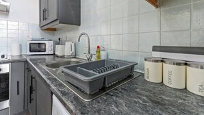 Eine moderne Küche mit Spüle, Mikrowelle, Wasserkocher und Aufbewahrungsbehältern mit den Aufschriften 'SUGAR' und 'COFFEE'.
