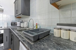 Een moderne keuken met een spoelbak, een magnetron, een waterkoker en opbergboxen met de aanduiding 'SUGAR' en 'COFFEE'.