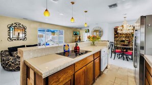 Una cocina moderna con una isla central, iluminación colgante y un comedor con candelabro.
