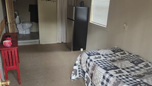 A compact room with a bed, a small desk, a refrigerator, a toilet, and a window. - Hunter's Shack - Bear Cabin (Mayhill)