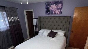 A bedroom with a bed, a ceiling fan, a door, and a wall with a floral painting.