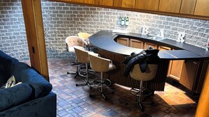 A compact kitchen with a bar area, featuring a brick wall, wooden cabinets, and a tiled floor.