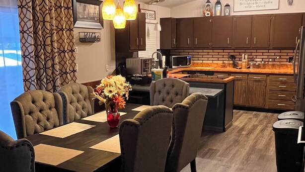 A modern kitchen with dark wooden cabinets, a central island, and a dining area with a long table and cushioned chairs.