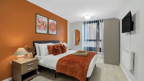 A modern bedroom with a bed, nightstand, and a mounted TV. - Modern 1BR • 2 min to Tube • O2 & ExCeL (London)
